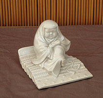 Antique Hirado porcelain figure, young priestess, possibly from a samurai family, sitting on an armor shoulder piece, wrapped in a thick shawl.